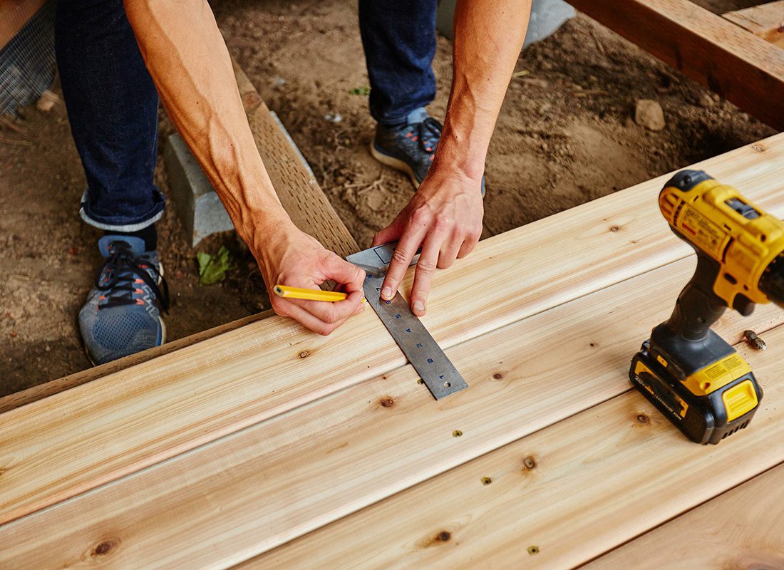 Insurance by Industry - Contractor Measuring Lumber While Building a Deck